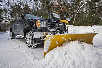 Truck with plow attachment during winter, pushing snow in a cleared lot.