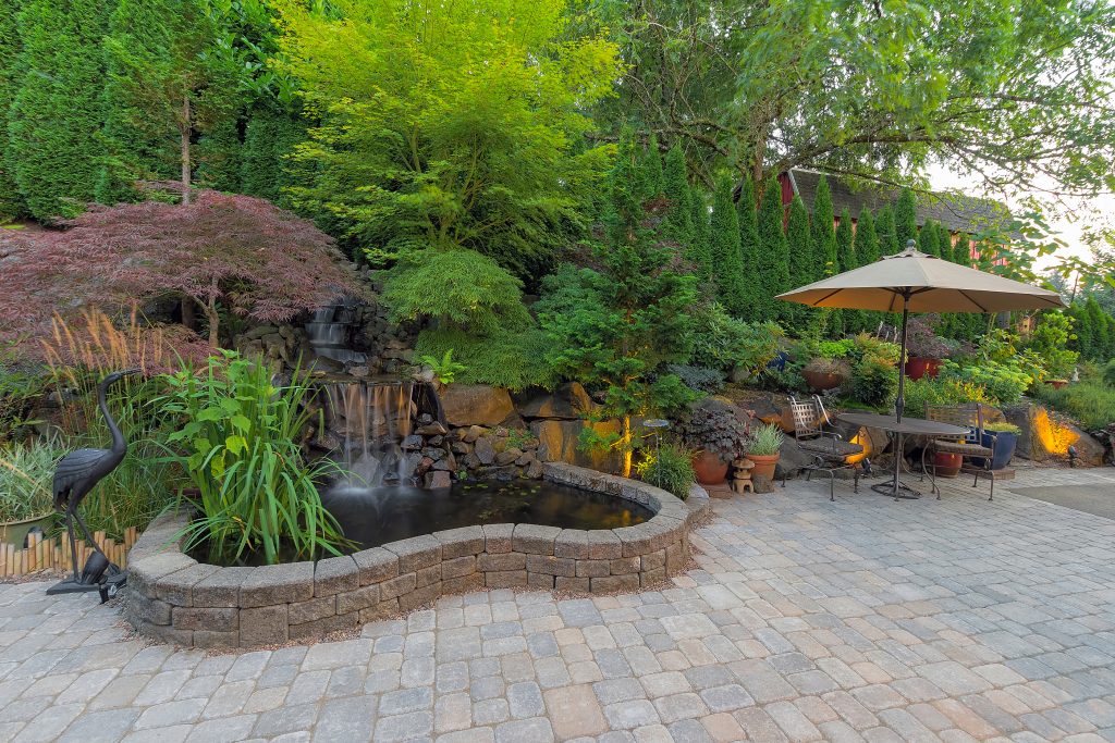 Hardscaped patio with other stonework and gardens in person's backyard.