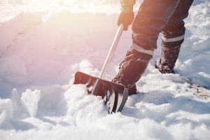 Worker shovels snow off a pathway with a snow shovel.